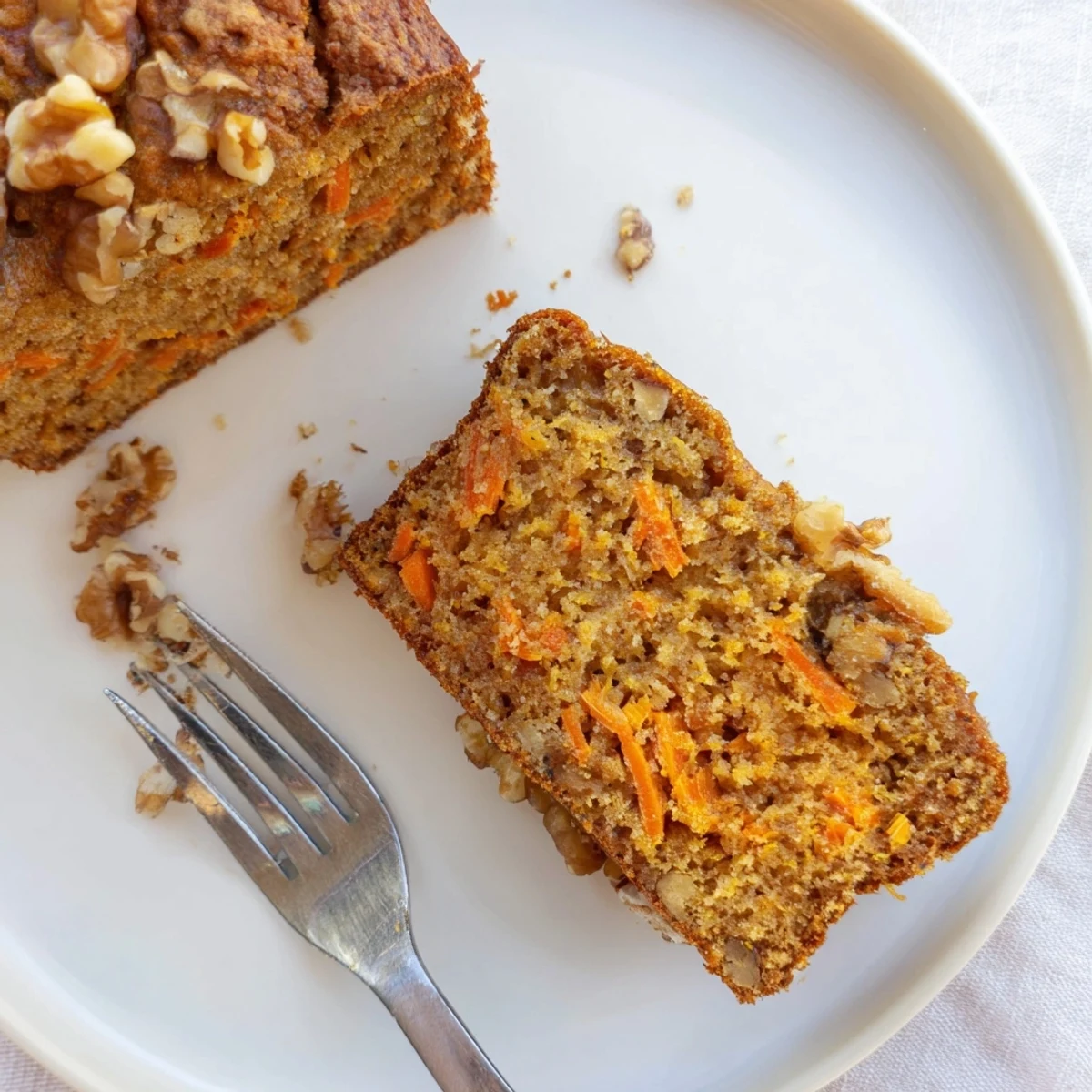 Warm slice of spiced carrot cake banana bread topped with walnuts and cream cheese glaze on a white plate