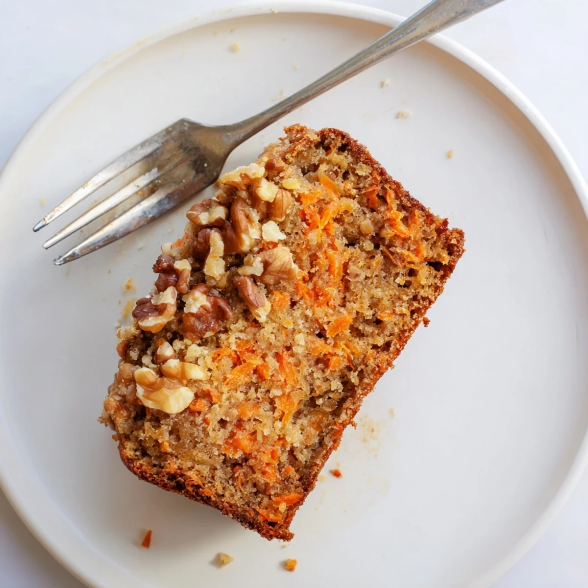 Golden brown carrot cake banana bread loaf with visible grated carrot specks and topped with cream cheese frosting on a wooden cutting board