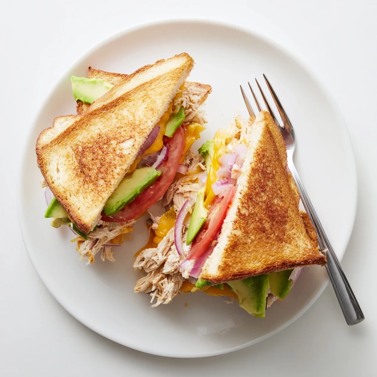 Golden brown chicken avocado melt sandwich with melted cheese oozing from toasted sourdough bread slices