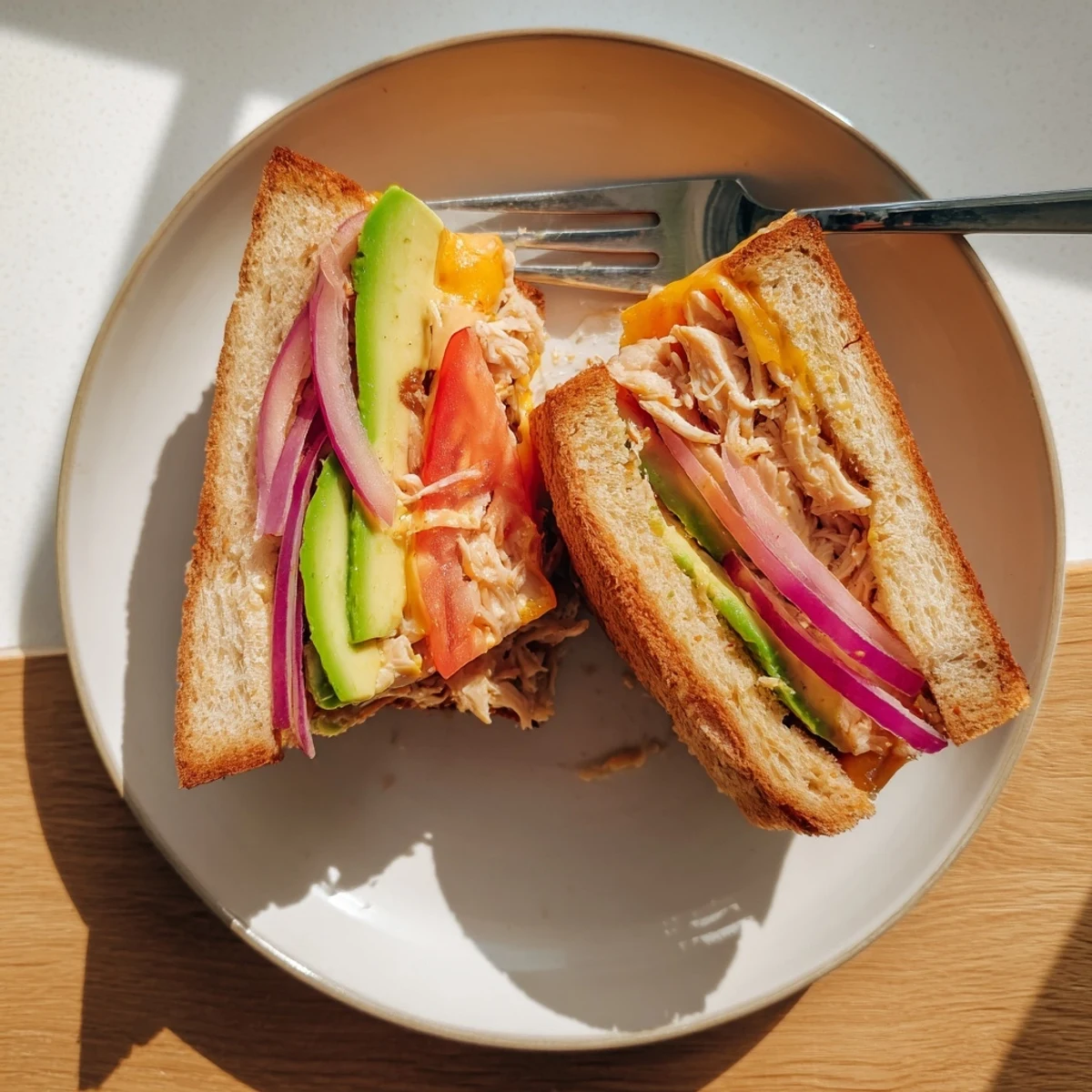 Warm chicken avocado melt sandwich served on a plate with tomato slices and melted cheese dripping from crispy bread