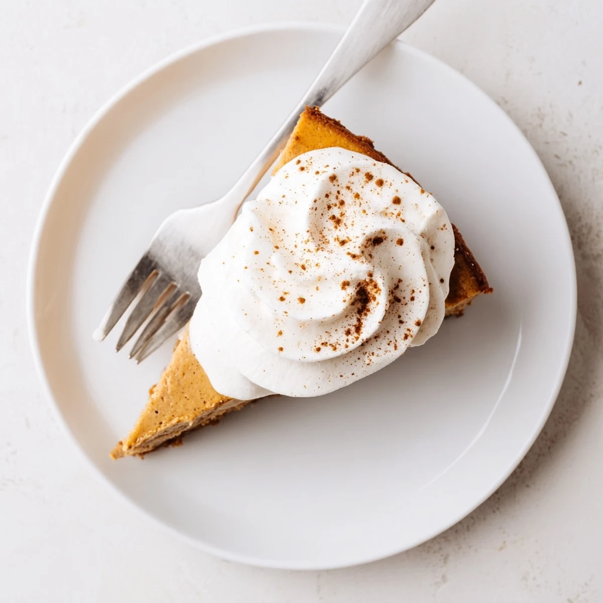 Creamy pumpkin spice Christmas cheesecake slice with whipped cream topping and cinnamon garnish