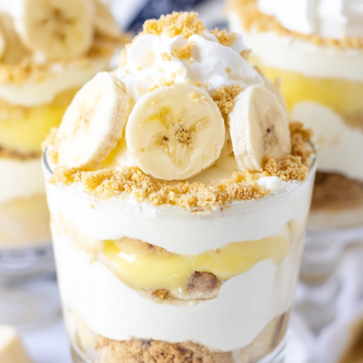 Golden vanilla wafer crust layers beneath silky no bake banana pudding cheesecake cups with fluffy whipped cream topping