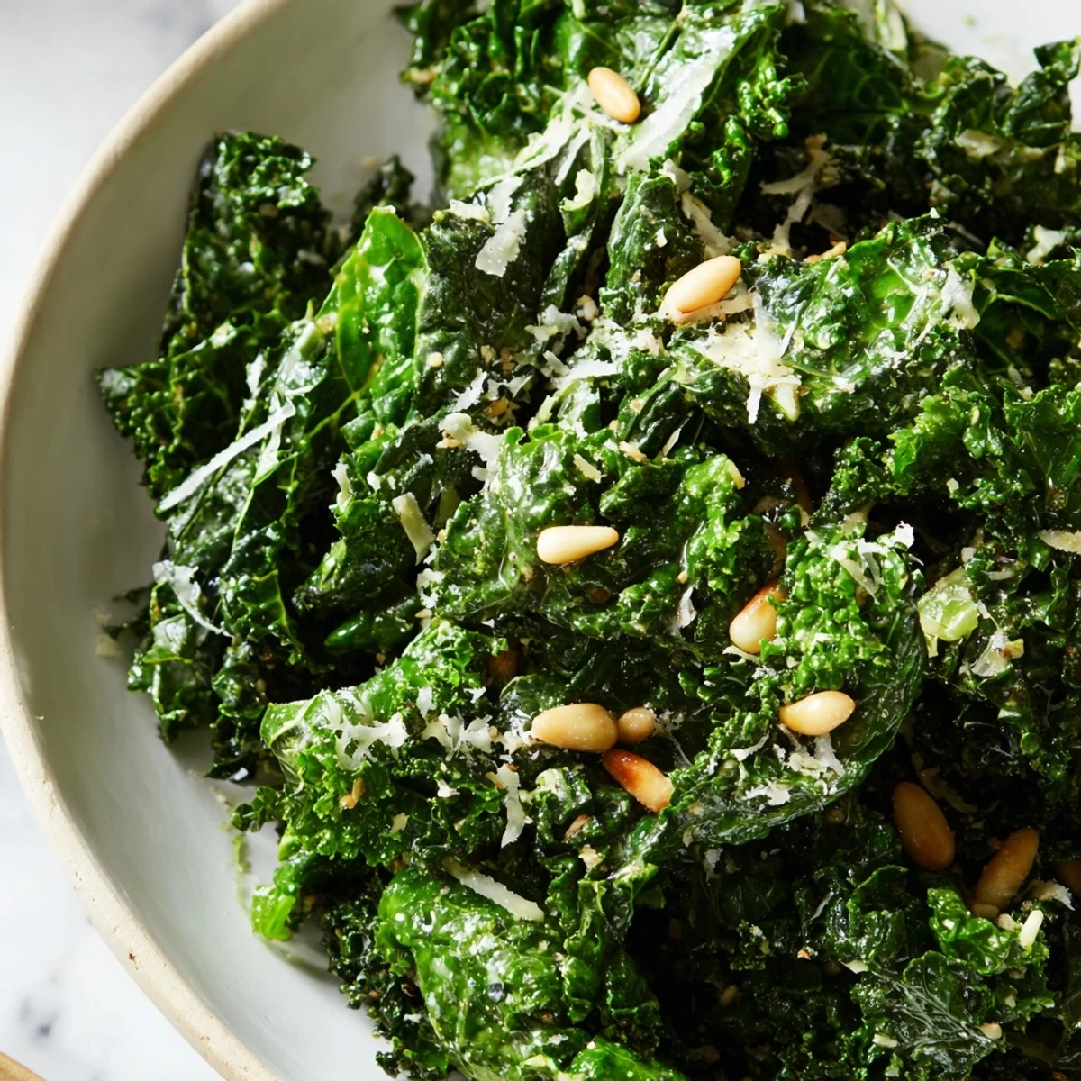 Garlic Lemon Parmesan Kale Salad in a white bowl with shaved cheese and toasted pine nuts