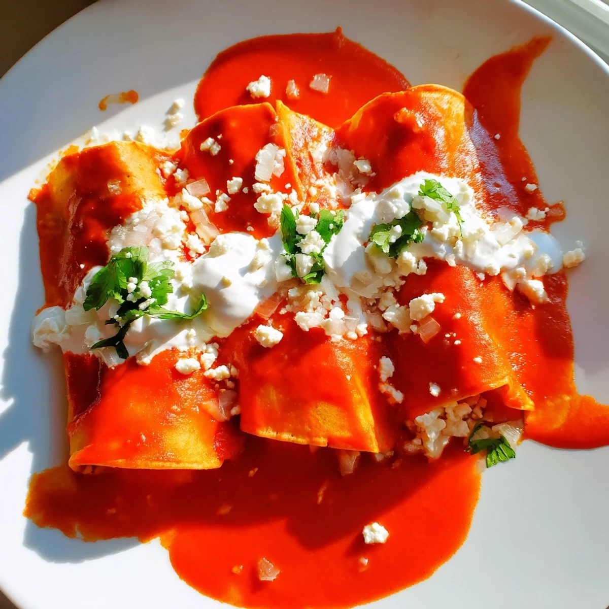 Entomatadas draped in rich red tomato sauce topped with crumbled queso fresco and fresh cilantro