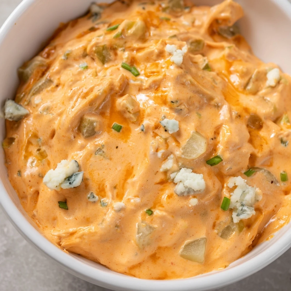 Creamy buffalo pickle dip in a serving bowl surrounded by crunchy chips and fresh veggie sticks