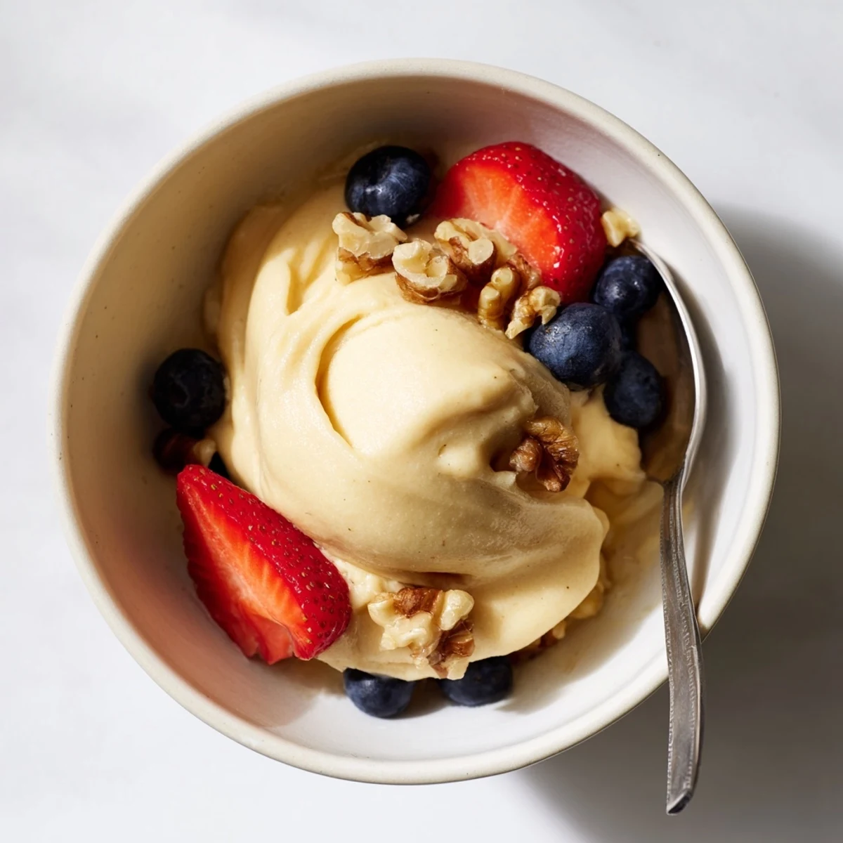 Creamy healthy nice cream recipe scooped into bowls topped with fresh fruit slices and chopped nuts