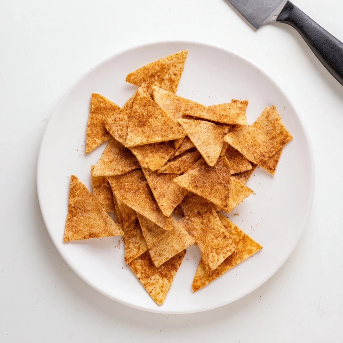 Gluten-free chickpea chips piled high on a white plate with scattered paprika