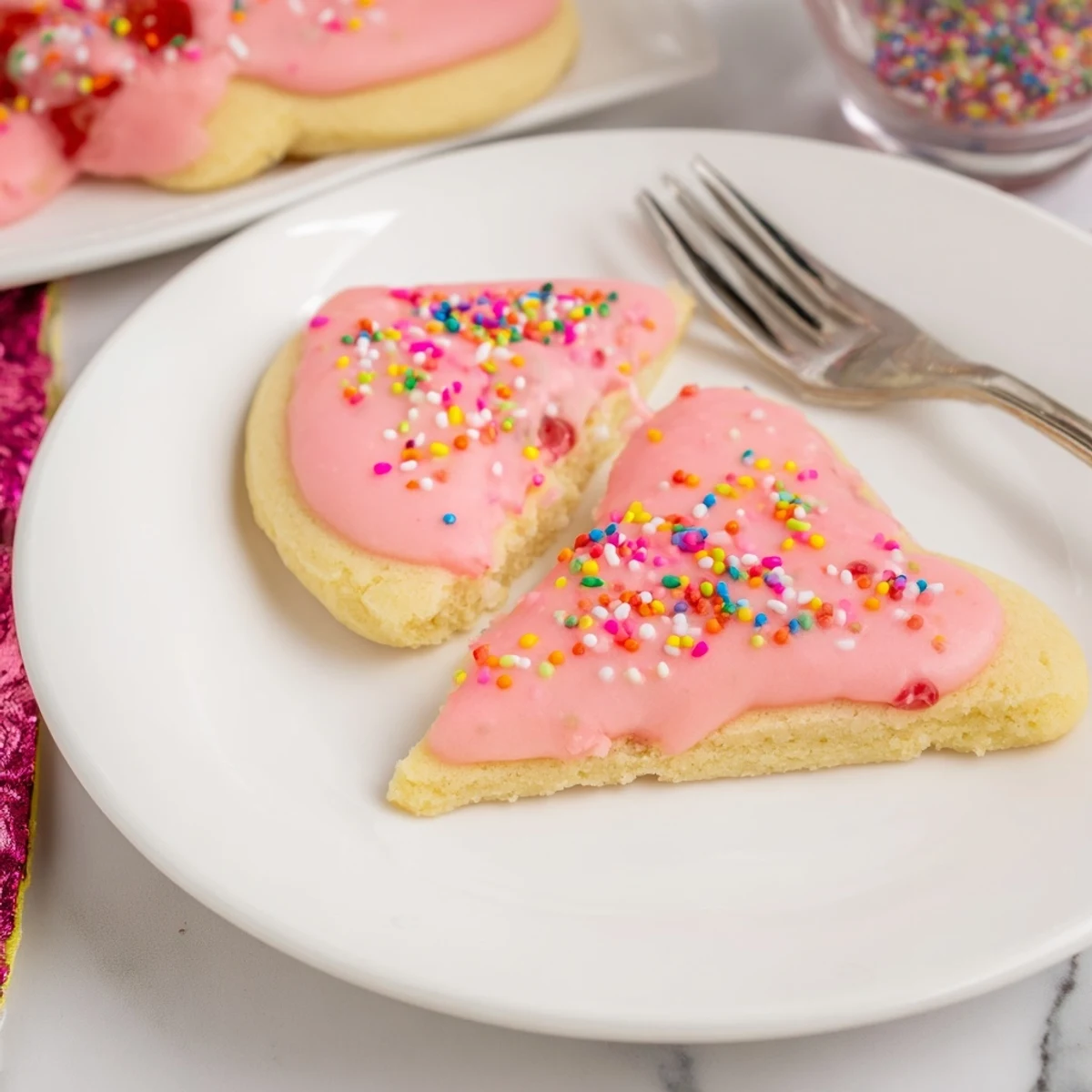 Golden Strawberry Pop Tart Cookies oozing with sweet jam and topped with pink vanilla glaze and rainbow sprinkles