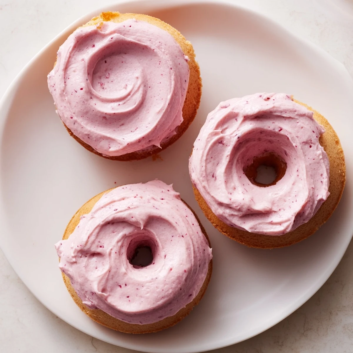 Golden baked strawberry buttercream frosted donuts with thick pink icing on a cooling rack