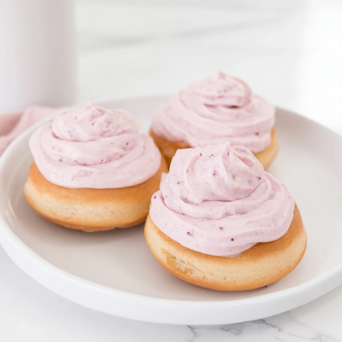 A plate of homemade strawberry buttercream frosted donuts drizzled with sweet berry glaze