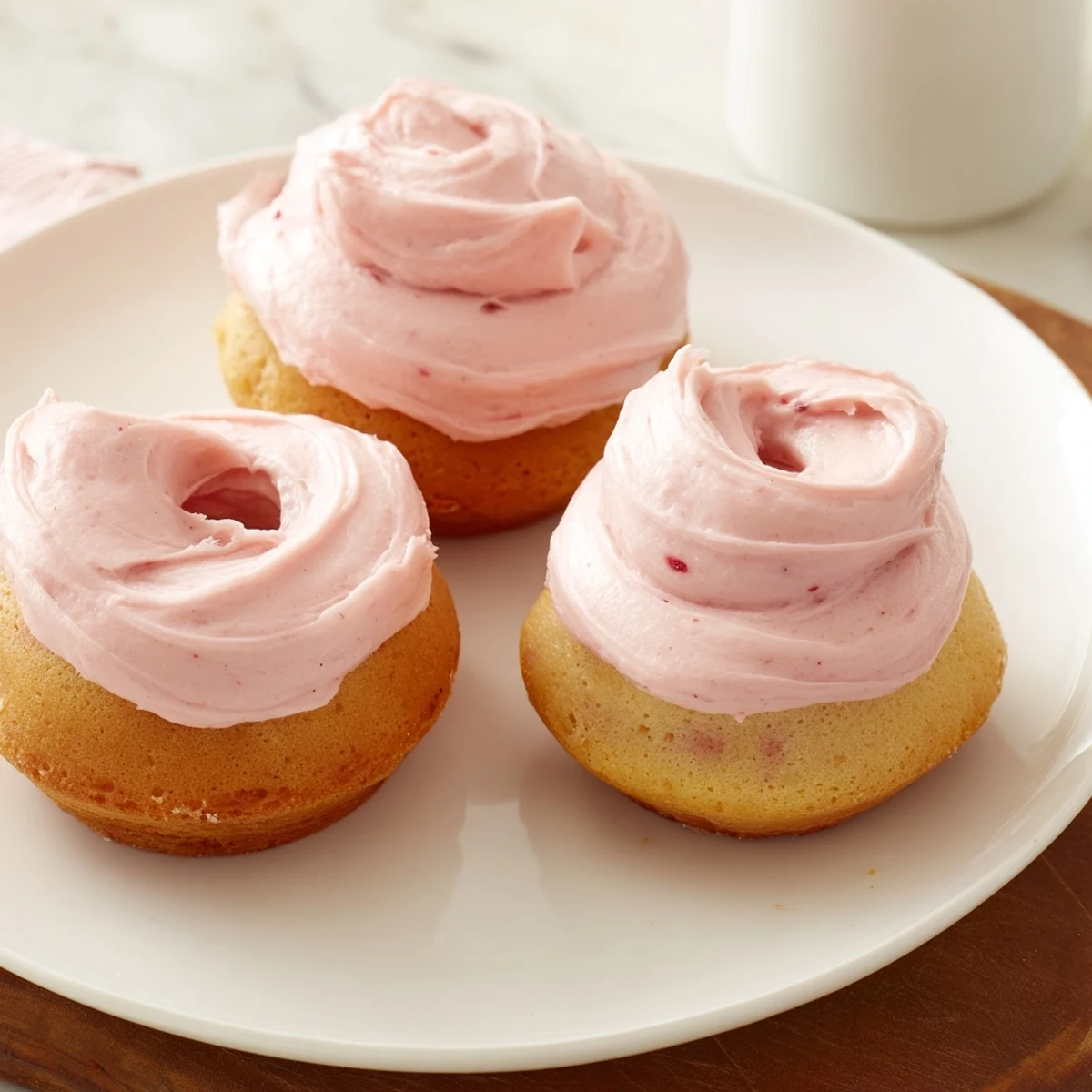 Strawberry buttercream frosted donuts topped with swirled frosting and scattered with colorful sprinkles