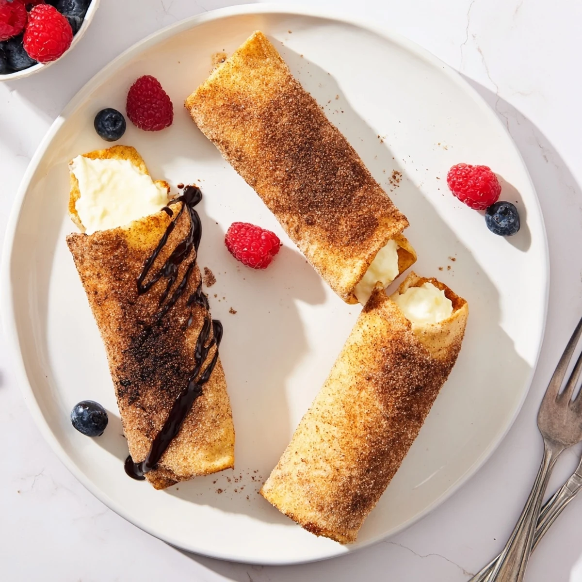 Crispy cheesecake chimichangas drizzled with chocolate sauce and fresh berries