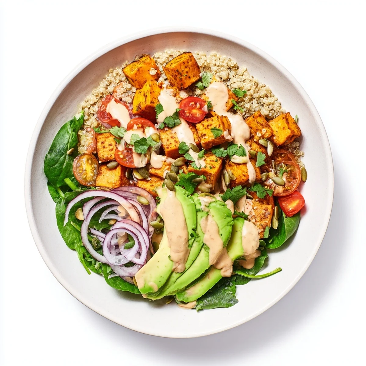 A vibrant sweet potato bowl with roasted cubes, avocado, and creamy tahini dressing drizzled on top