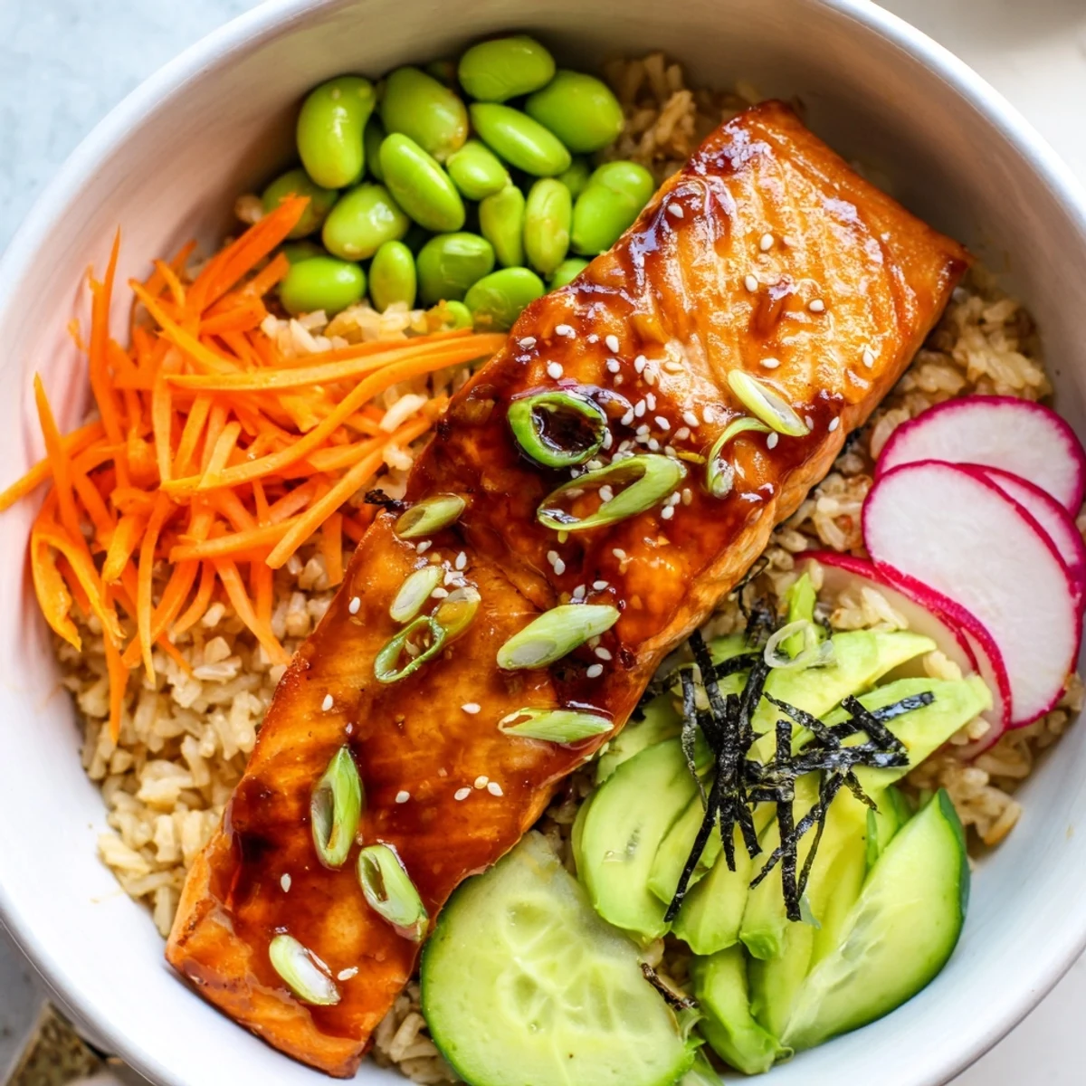 Miso salmon grain bowl drizzled with tangy dressing beside fresh avocado slices