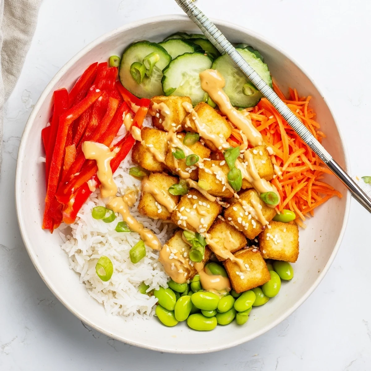 Crispy golden tofu rice bowl with peanut sauce drizzled over colorful fresh vegetables