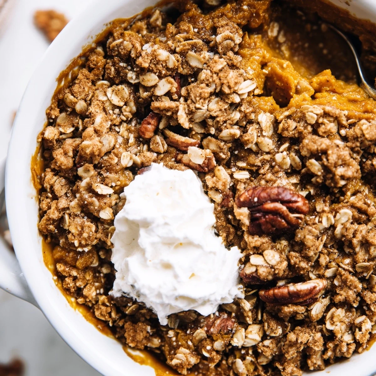 Warm pumpkin pie crisp scooped into a bowl with whipped cream on top