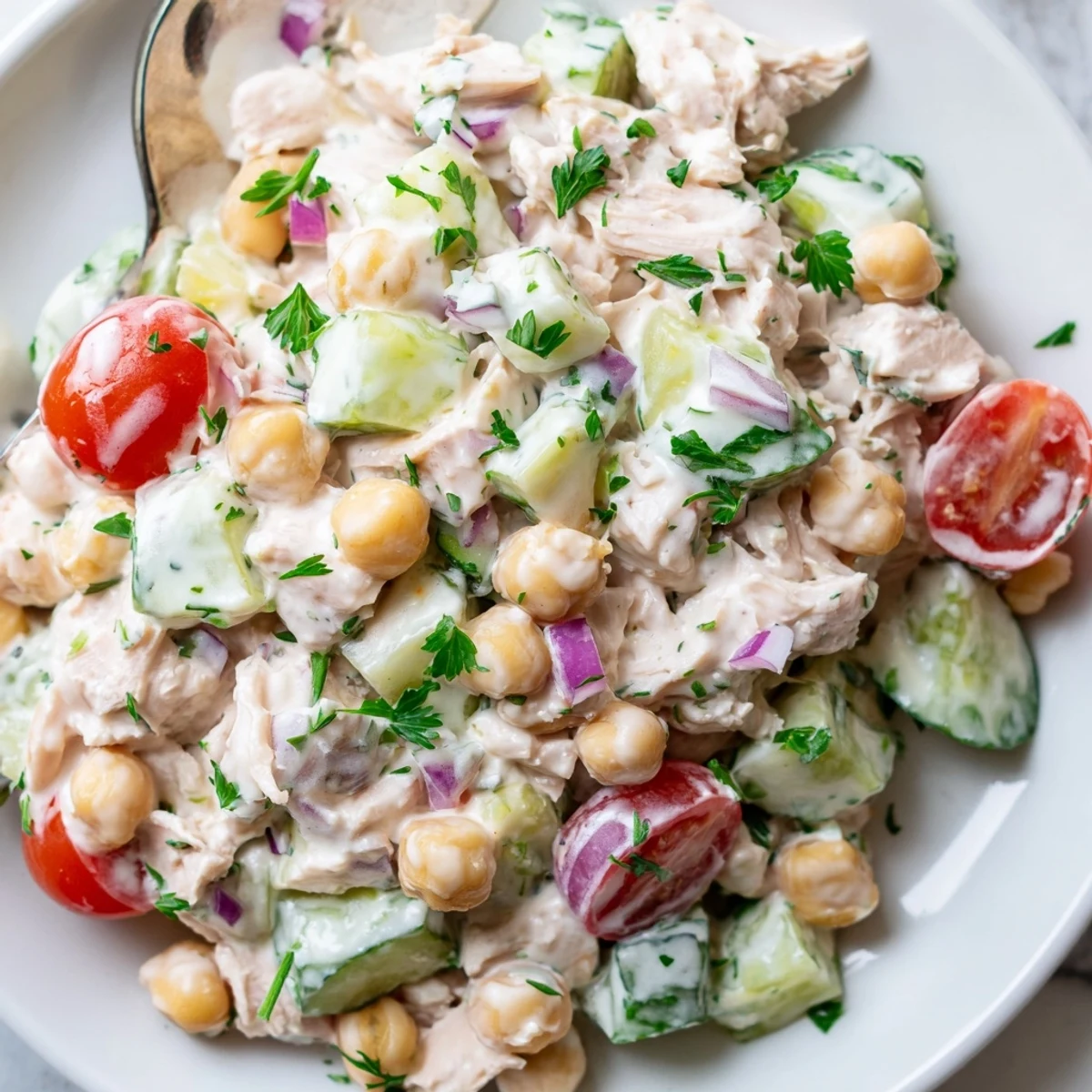 A close-up of creamy tuna chickpea cucumber salad studded with ripe cherry tomatoes