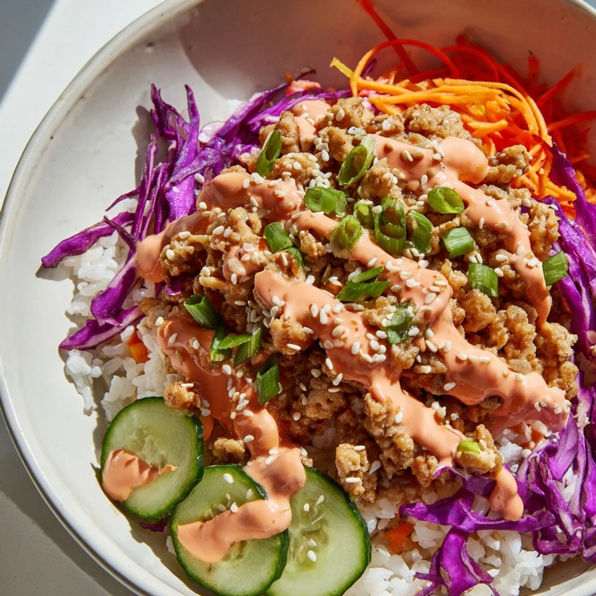 Colorful ground turkey rice bowls topped with shredded carrots, cabbage, and sweet chili sauce.