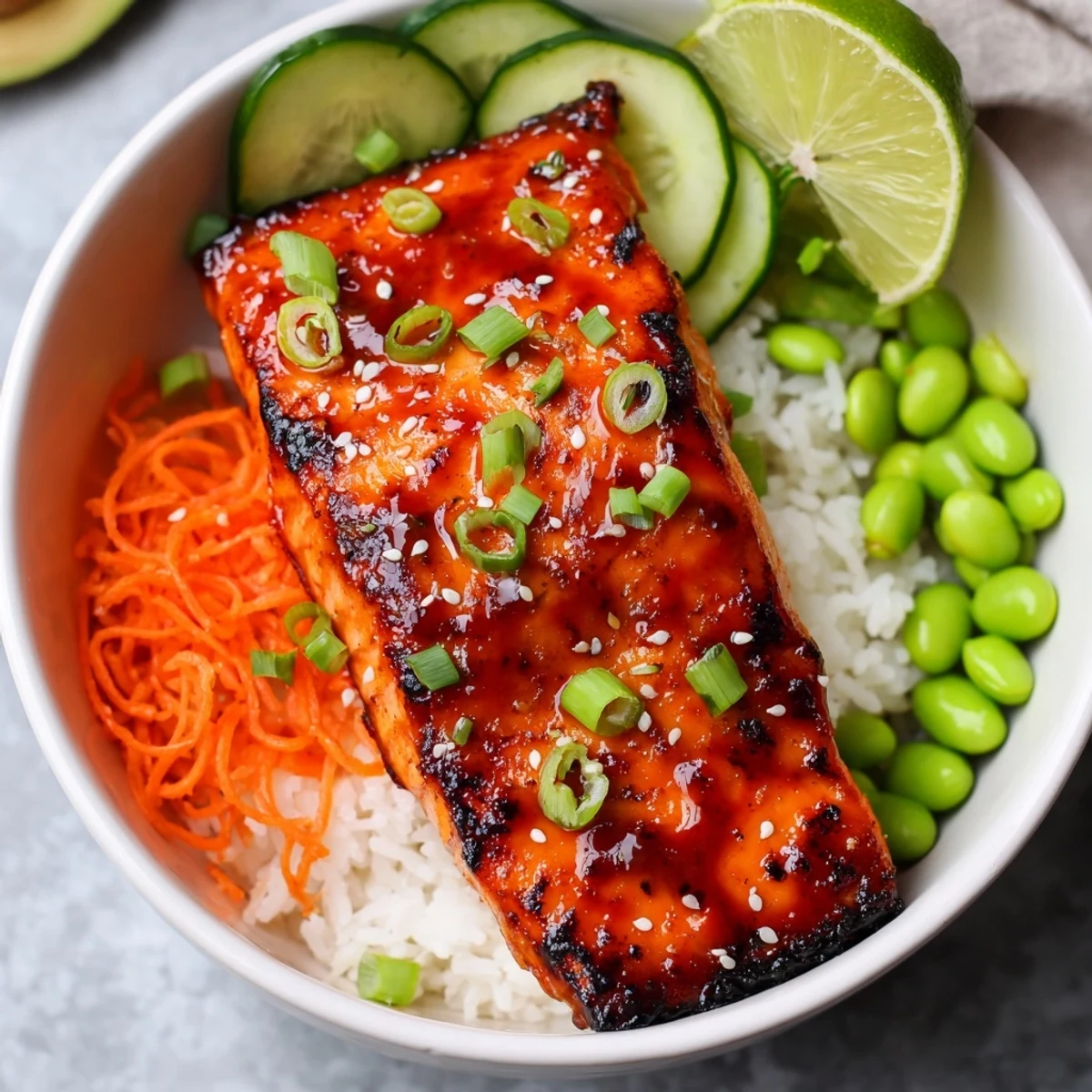 Glossy Sriracha Honey Glazed Salmon Bowls topped with sesame seeds and fresh lime wedges