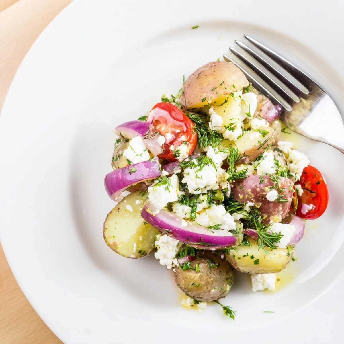 Golden potato and feta salad garnished with dill, olive oil, and red onion