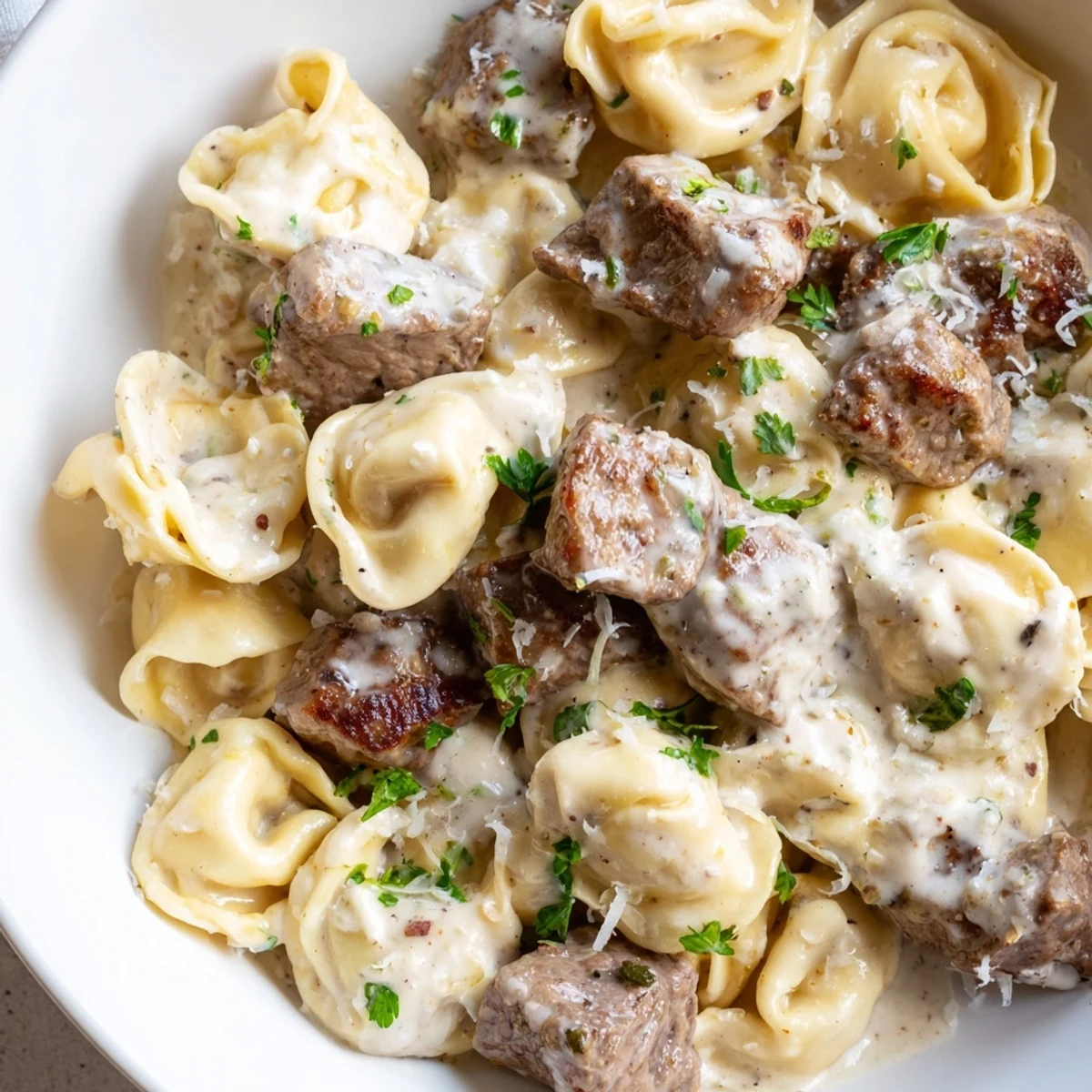 Creamy garlic steak tortellini plated in a white bowl with fresh parsley garnish