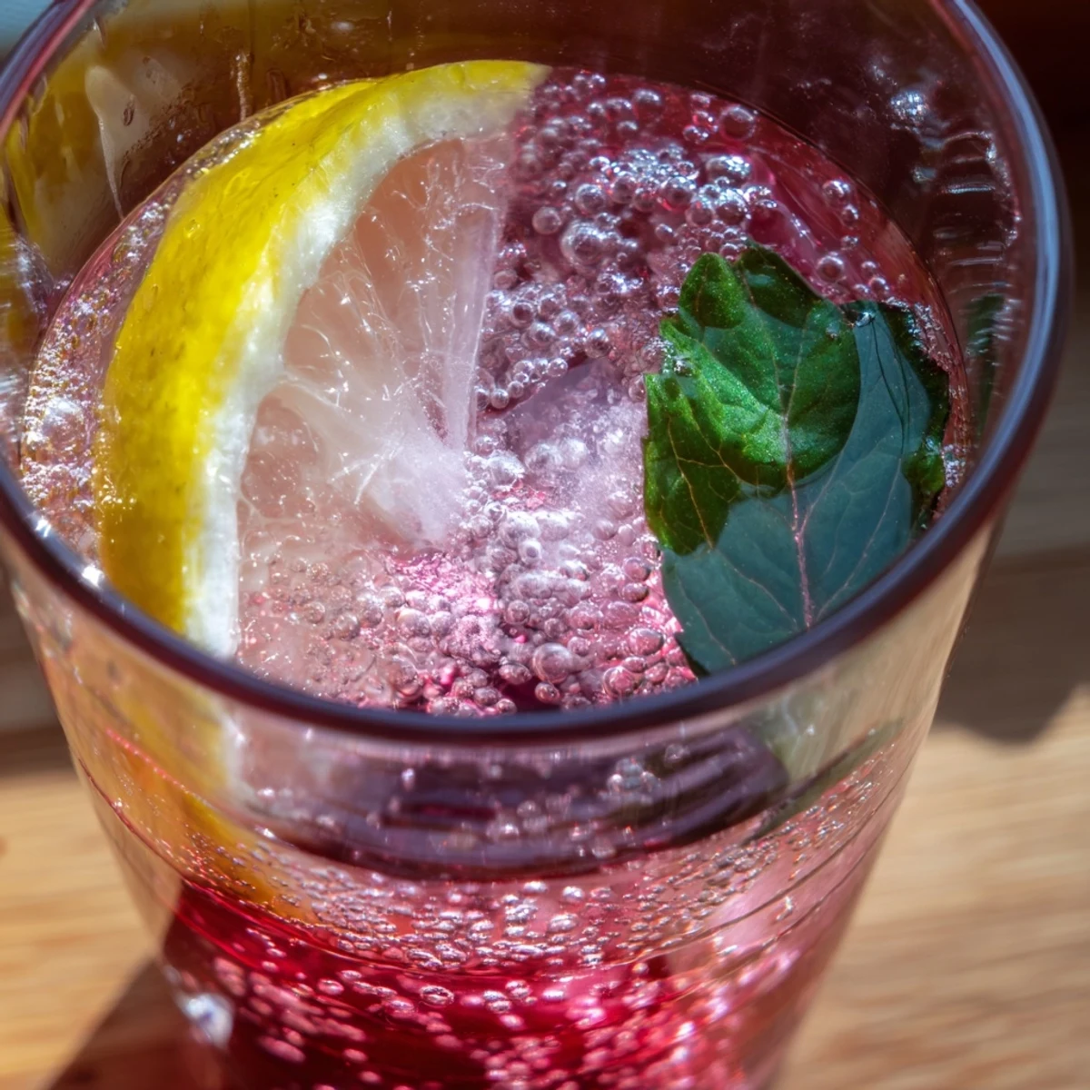 Glass of chilled refreshing honey lemon pink soda bubbling with lemon slices and ice  